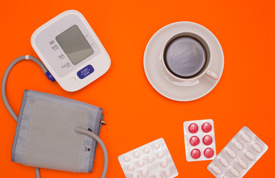 The concept of health, the effect of coffee on blood pressure. Electronic blood pressure tonometer, a Cup of coffee and pills on a bright orange background. The view from the top.