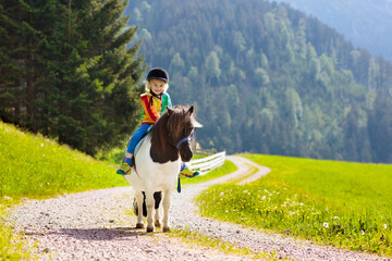 Kids riding pony. Child on horse in Alps mountains