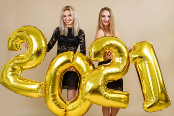 Beautiful Blonde Models Celebrating New Year. Happy young women with golden 2021 balloons on beige background