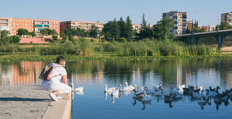 Obraz premium Rear View Of A Beautiful Young Girl On A Jetty Looking At The Ducks In The River. Woman with a protective mask due to Covid-19.