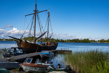 an old northern ship with a mast and sails stands near the pier