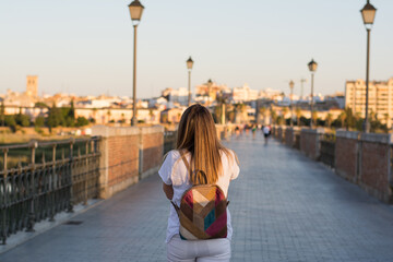 Fototapeta premium Rear view of a woman walking through the city using her mobile phone.