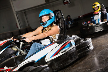 Glad cheerful positive girl and her friends competing on racing cars at kart circuit