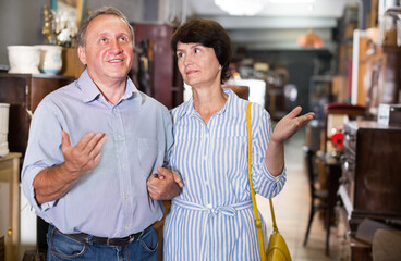 Fototapeta na wymiar Mature man with his wife are choosing furniture in a antique shop. Focus on man