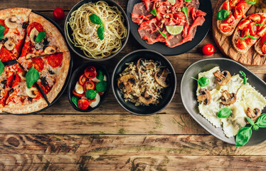 Table of italian meals on plates Pizza, pasta, ravioli, carpaccio, mushroom risotto, caprese salad and tomato bruschetta on rustic wooden background.