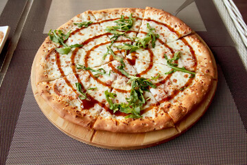 Pizza with arugula on a wooden plate on grey background in summer terrace