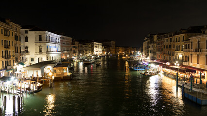 Nightly scene overlooking a canal with boat traffic in Venice. Some restaurants are waiting for customers.