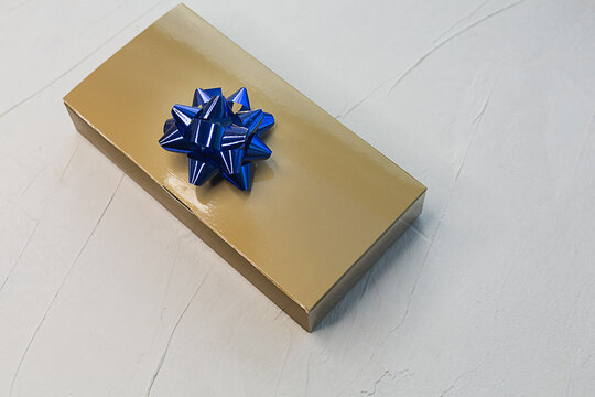 Golden Box With A Gift And A Blue Bow On A Light Texture Background.