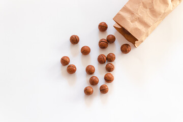 Flat composition with macadamia nuts scattered from paper bag on a white table