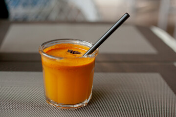 Autumn drink in glass with tube and piece of star anise on the outdoor terrace. Sea-buckthorn smoothie