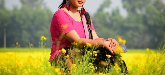 A young lady portrait sitting in a mustard field in a sunny daylight outdoor
