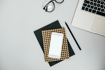 Fototapeta premium Top view of office desk with laptop computer, mobile phone with blank space, notebook, pen and glasses flat lay stock photo
