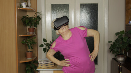 Grandmother in virtual headset glasses watching video in VR helmet and training workout at home