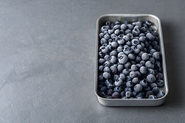 Frozen blueberries in a metal tray on a concrete background.