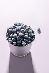 Frozen blueberries in a metal pot on a pink background.