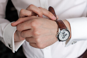 a man in a white shirt adjusts his watch on a brown strap