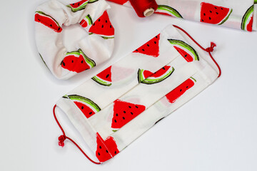 Top view on handmade fabric cotton reversible face mask and hair scrunchie in white with watermeloon pattern. Protection against saliva, cough, dust, pollution, virus, bacteria, coronavirus, COVID-19.
