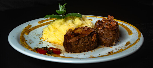 Filet mignon with fried onion and mashed potato, decorated with cherry tomatoes and mustard sauce on black background.