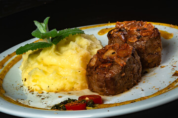 Filet mignon with fried onion and mashed potato, decorated with cherry tomatoes and mustard sauce on black background.