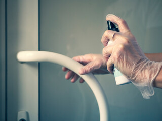 Woman hands in gloves is applying sanitizer on the door handle. Antiseptic treatment of door...