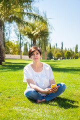 pretty middle-aged woman sits on the grass under palm trees with a smartphone. work online in retirement. lifestyle