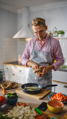 Handsome Young Man Preparing a Healthy Vegetarian Meal on a Frying Pan. Sprinkling Healthy Green Food with Herbs and Spices in a Modern Kitchen. Natural Clean Diet and Healthy Way of Life Concept.