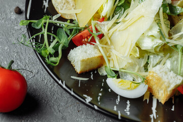 Fresh Caesar salad in a black plate on a gray background.Top view