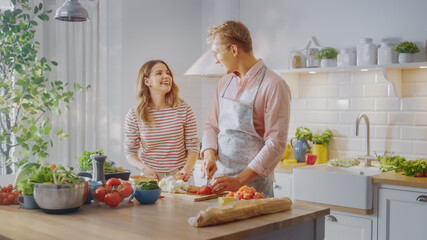 Handsome Young Man in Glasses Wearing Apron and Beautiful Girl are Preparing a Salad in the Kitchen. Happy Couple are Casually Talking. Natural Clean Diet and Healthy Way of Life Concept.