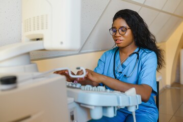 Smiling African woman doctor with ultrasound scanner in hand, working on modern ultrasound scanning machine in light room in clinic. Portrait Of 4D Ultrasound Scanning Machine Operator