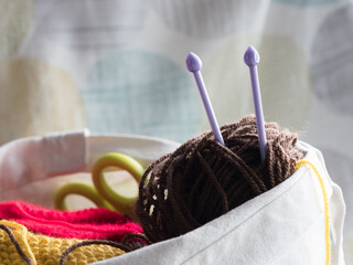 A bag contains wool and scissors and two needles poking out of a ball of wool.