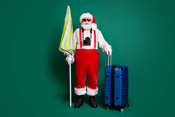 Full length body size view of nice handsome bearded funky cheerful overweight fat Santa carrying parasol valise air flight fly departure wearing digital camera isolated over green color background © deagreez