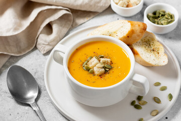 Pumpkin soup. Pumpkin cream soup in a white plate on the light gray kitchen table. Vegetarian autumn soup close up