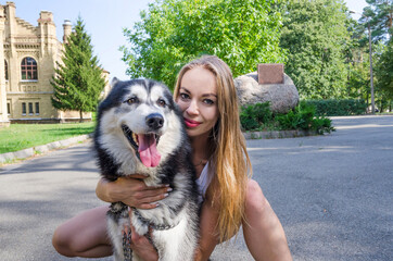 Naklejka na ściany i meble young beautiful girl hugs a husky dog and looks into the camera.