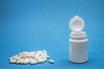 White bottle with a pile of oval tablets on a blue background. Background