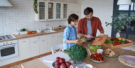 Healthy eating. Young dad and his little son cutting preparing a vegetarian salad while standing in the modern kitchen at home, spending time together