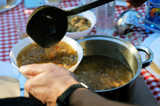 Man pouring traditional polish soup flaki "tripe" into a bowl at a garden party
