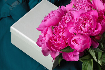 bouquet of pink flowers and a gift in the hands of girl. Gray square box and pink peonies on emerald background
