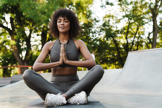 Image of african american sportswoman meditating while working out