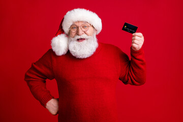 Photo positive grey beard old man santa claus headwear hold credit card recommend buy wish x-mas gift with easy bank payment wear sweater jumper isolated bright shine color background