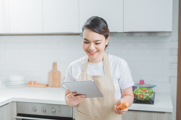 beautiful korean woman in apron holding tablet pad looking at list and checking fresh vegetables