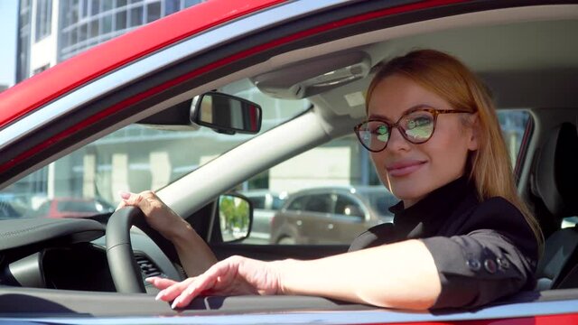 Attractive stylish woman with long hair in luxury car on a building background. Auto business, technology and people concept