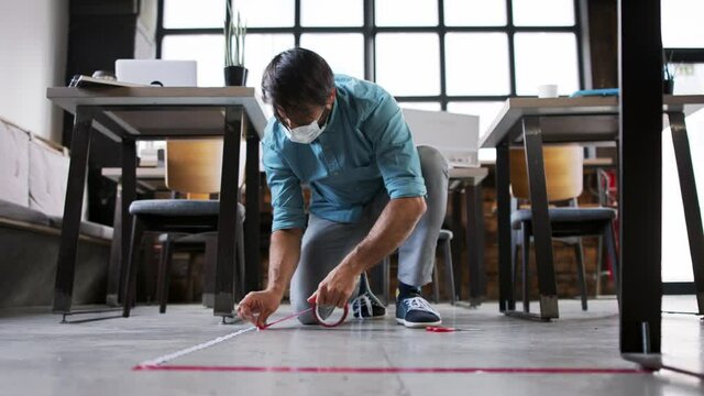 Young businessman with face mask working indoors in office, marking safe distance.