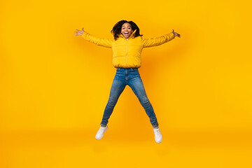 Fototapeta na wymiar Joyful African Girl Doing Spread Eagle Jump Over Yellow Background