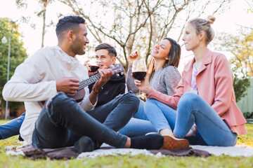 Cool friends enjoying at the sunset.  Playing ukulele and drink wine.  Unfocused photography with sunshine. The focus is on the man behind.