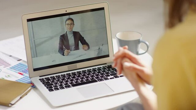 Over the shoulder shot of unrecognizable woman talking on video call with colleague while working from home