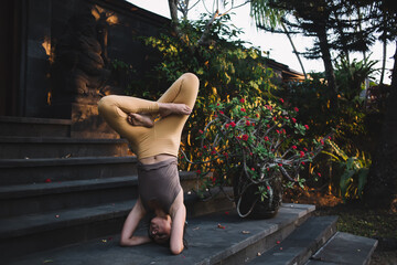 Young woman doing yoga headstand on stairs among beautiful greenery