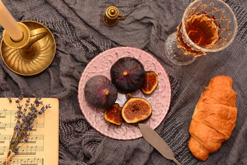  Composition of plate with ripe figs, glass of wine, croissant, candlestick on gray cloth background top view.  composition, mood. 