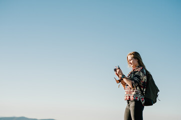 Hiker tourist in the mountains at sunset. Girl takes pictures of the sunrise. Hipster girl with a camera and a backpack travels and enjoy nature.