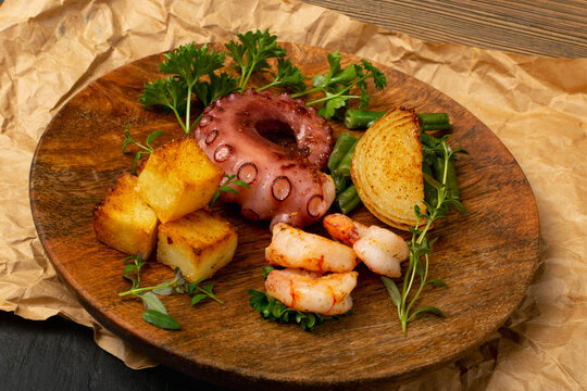 Grilled octopus tentacle on a wooden plate served with shrimps