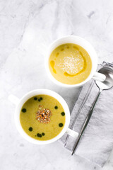 Zucchini and peas cream soup in bowls on light marble table background. Top view, copy space